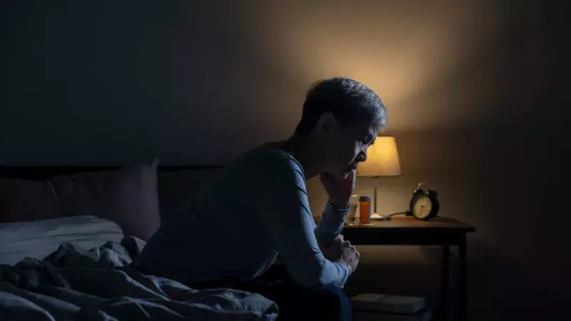 Une femme de type asiatique est assises sur son lit dans la pénombre.